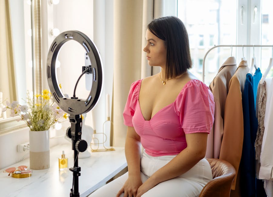 Young woman in pink top setting up camera for video recording with ring light indoors.