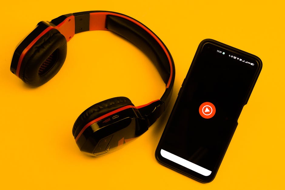 Wireless headphones and smartphone with play icon on a vibrant yellow background.