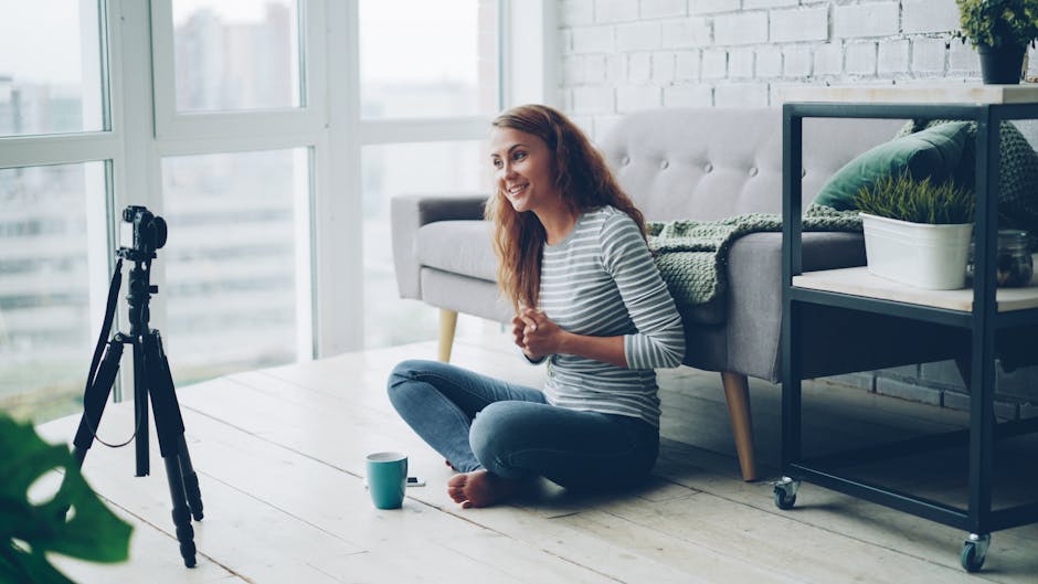Smiling woman sitting on the floor vlogging with camera tripod in a modern living room.