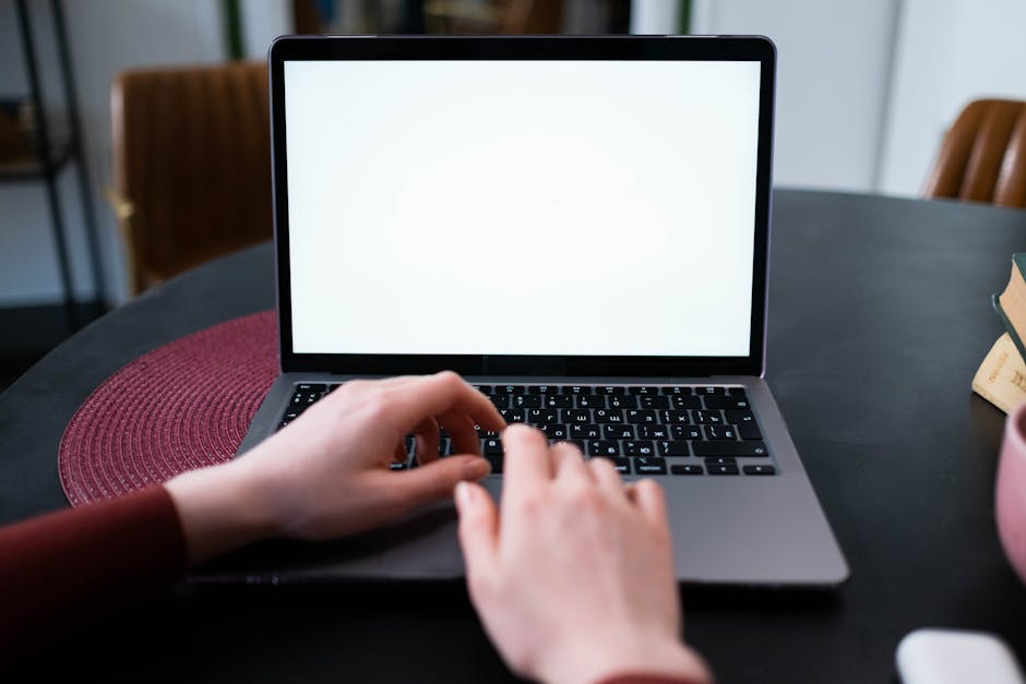 Hands typing on a laptop keyboard with a blank white screen on a round table.