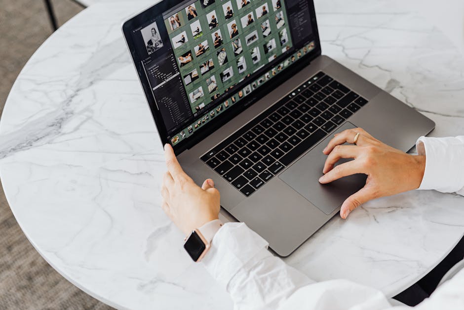 Hands editing photos on laptop, modern workspace on marble table.
