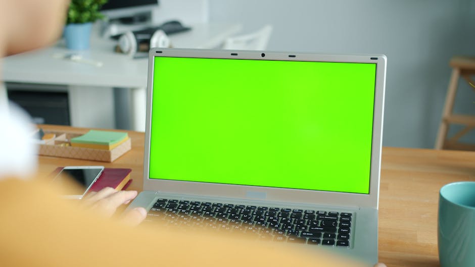 Person working on a laptop with a green screen in a modern office setting.