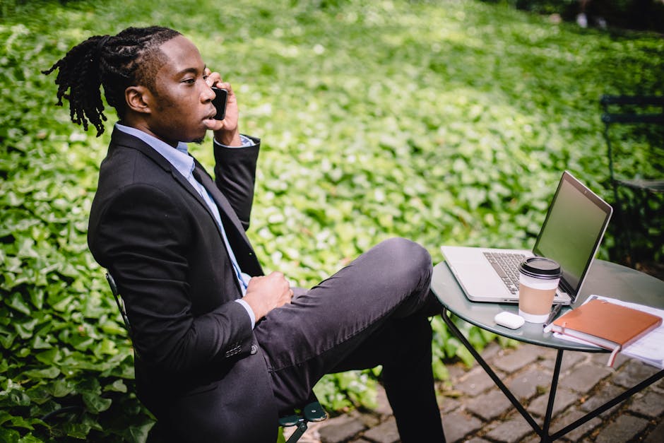 Young businessman working outdoors on laptop while taking a phone call.