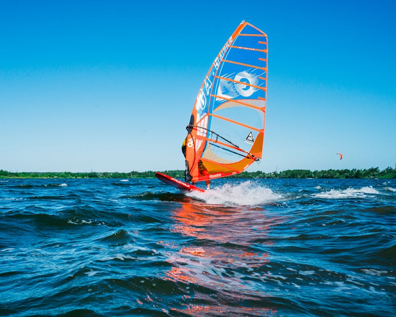 Experience the thrill of windsurfing on vibrant blue waters with clear skies in this dynamic image.