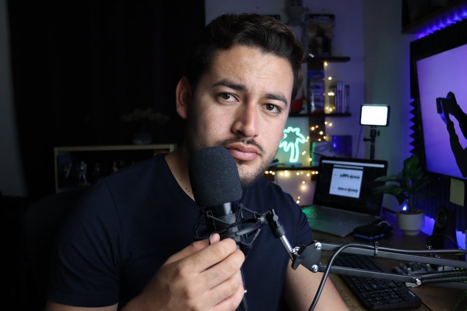 Man in a studio setting, talking into a microphone with a focused expression.