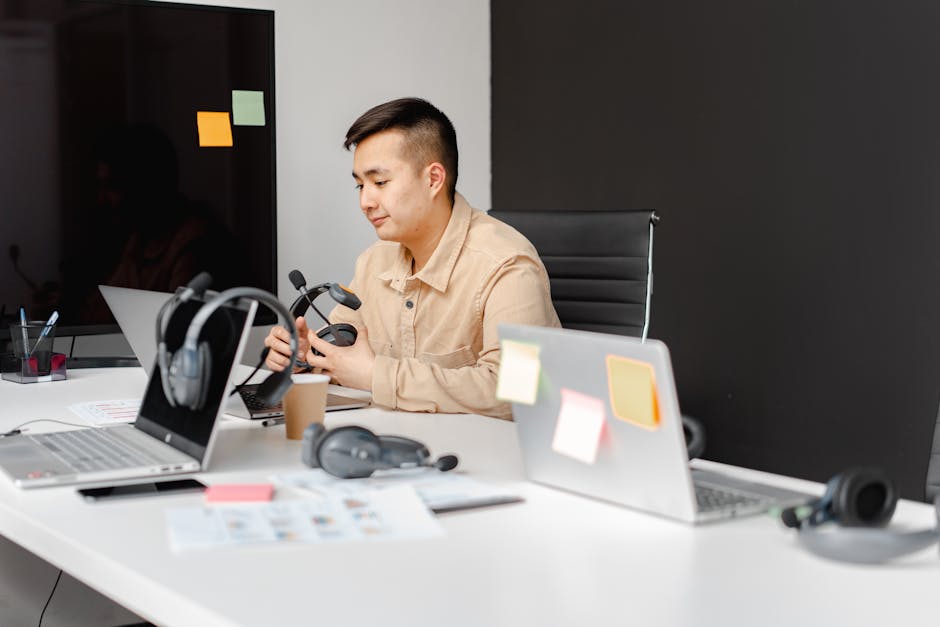 Asian man in an office setting using a laptop and headset, symbolizing customer service or remote work.