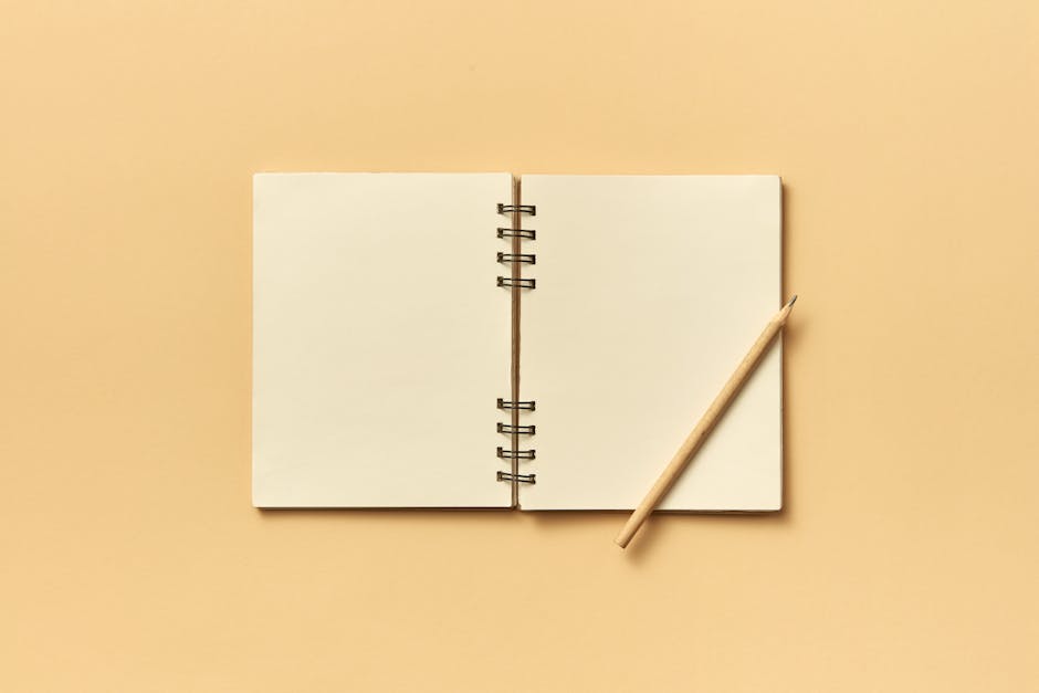 An open spiral notebook with a pencil on a neutral beige background, perfect for creative projects and planning.