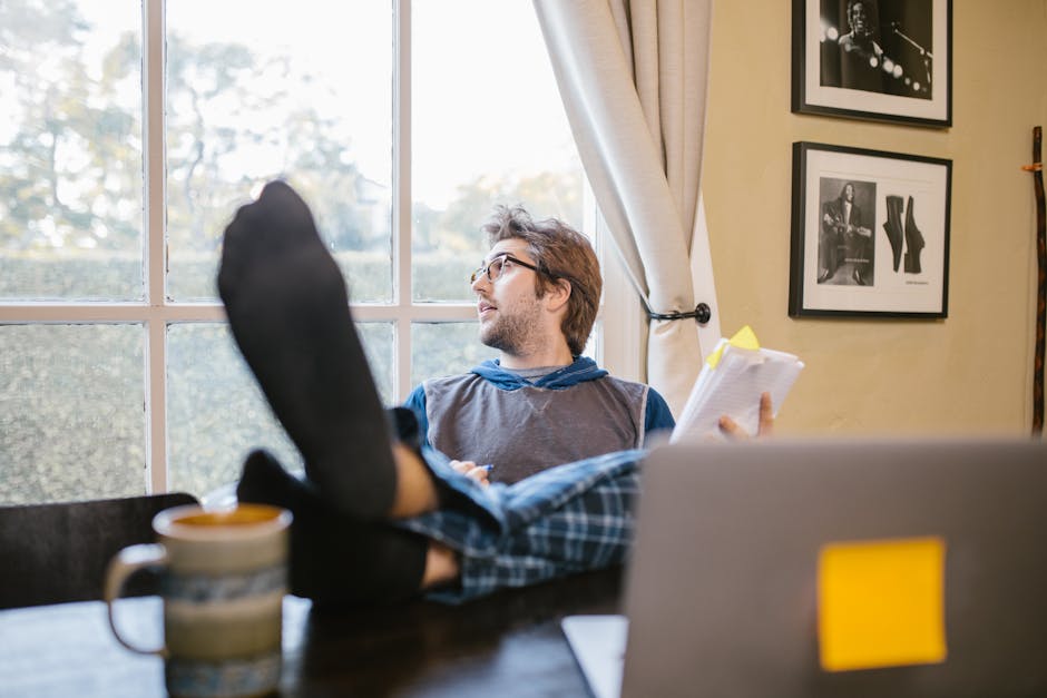 Man enjoying a relaxed home office setup with feet up, looking out the window.
