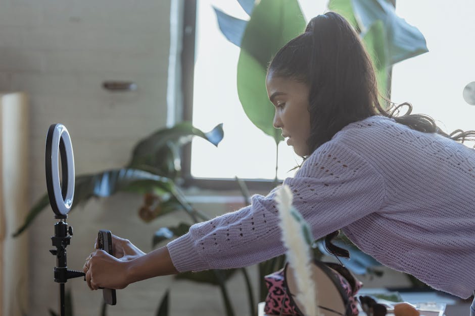 Focused young woman adjusts smartphone tripod for video shoot indoors.