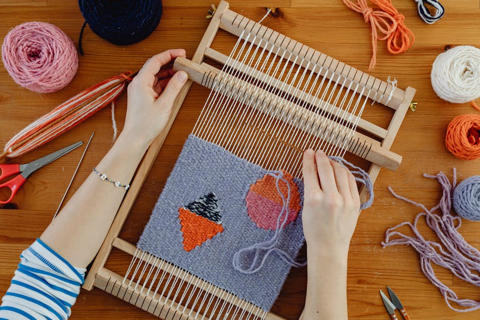 Close-up of hands weaving colorful patterns using a loom and yarn on wooden surface.