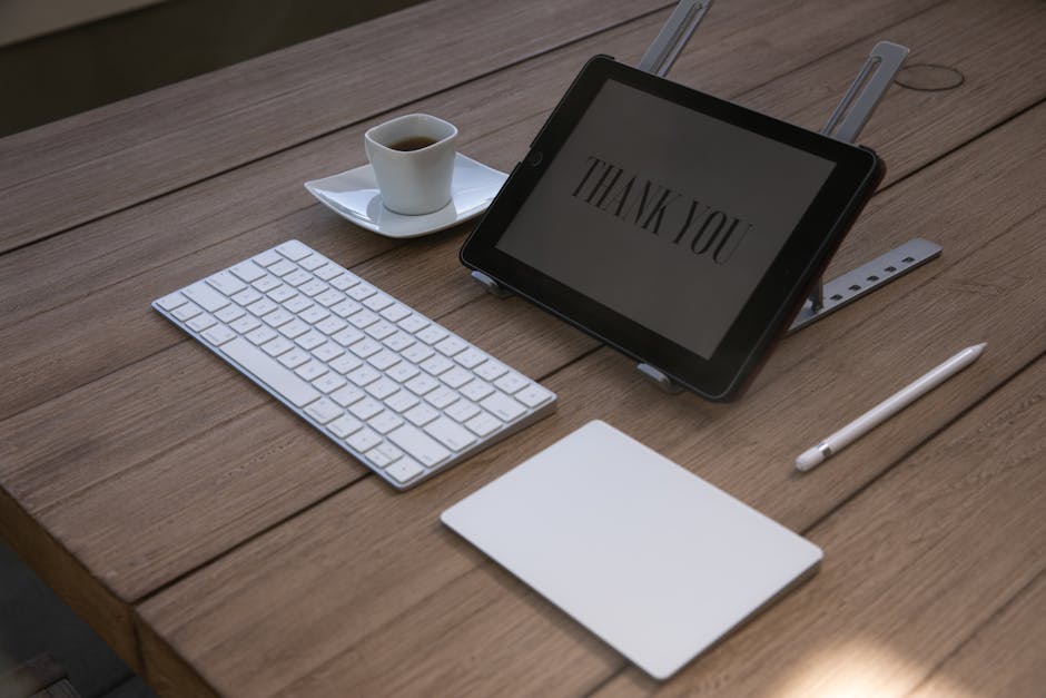 A contemporary workspace features a tablet displaying 'Thank You', a keyboard, an Apple pencil, and a coffee cup on a wooden desk.