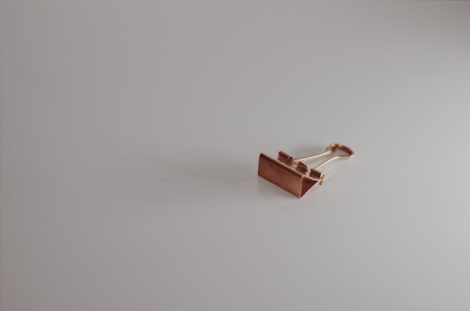 A single rose gold binder clip placed on a clean, white surface. Minimalist and modern aesthetic.