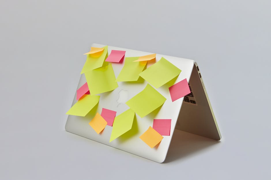 Open laptop covered with colorful sticky notes on a gray background, symbolizing organization.