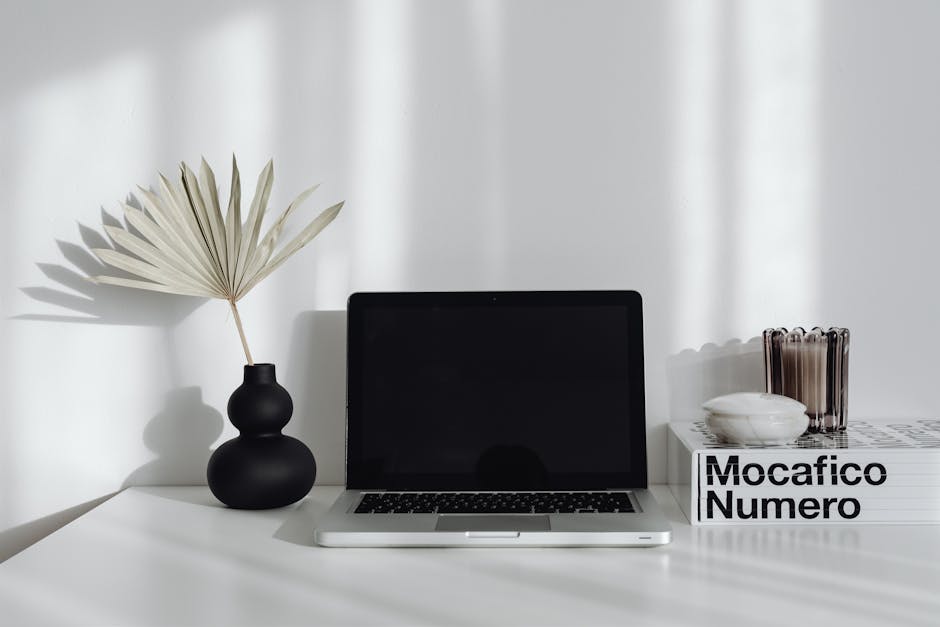 A minimalist desk setup featuring a laptop, a decorative vase, and books, creating a modern workspace feel.