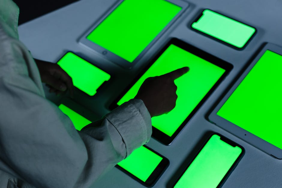 Person interacting with multiple green-screen electronic devices indoors.