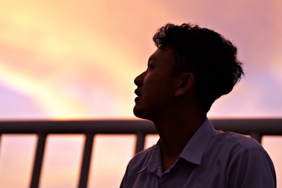 A man's silhouette against a colorful sunset sky, capturing a contemplative moment outdoors.